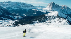 Skiers on a snowy mountain slope with rugged peaks in the background